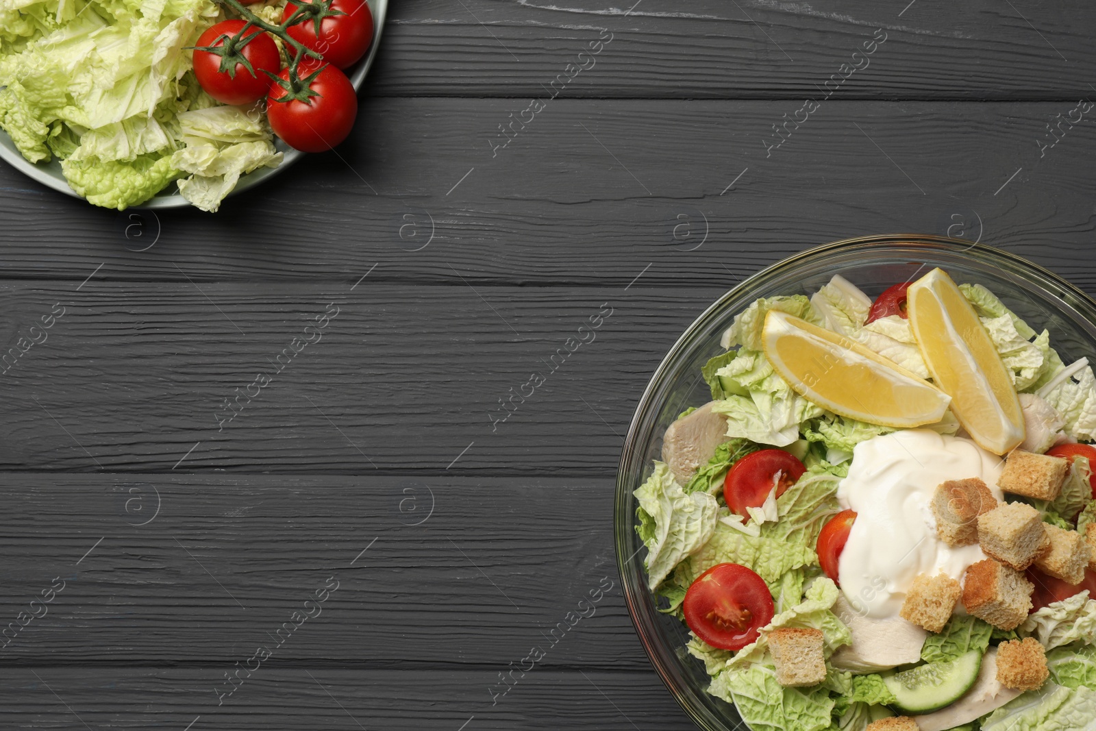 Photo of Bowl of delicious salad with Chinese cabbage, lemon, tomatoes and bread croutons on black wooden table, flat lay. Space for text