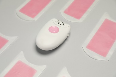 Photo of Modern epilator and wax strips on light grey background. Hair removal