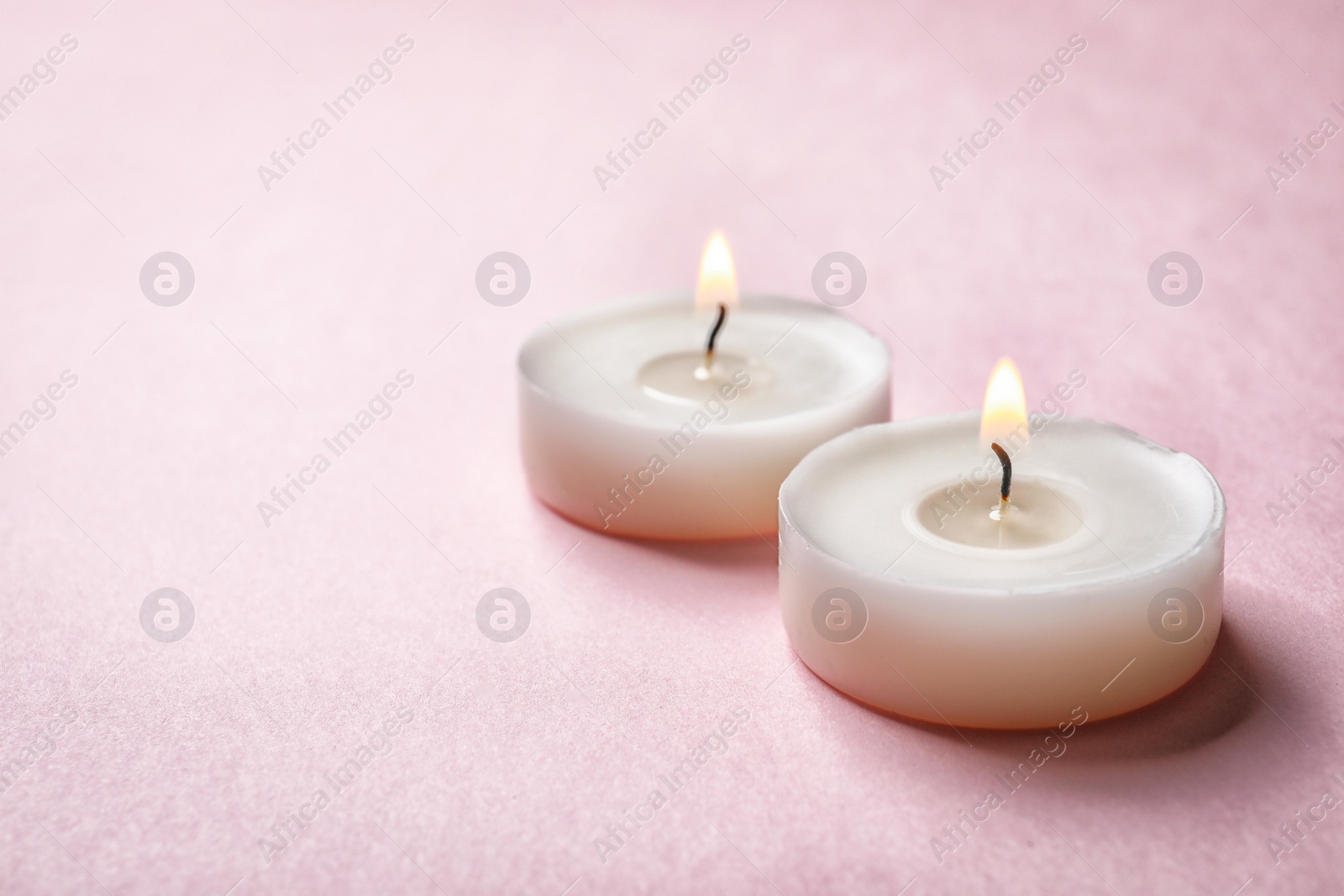 Photo of Small wax candles burning on color background