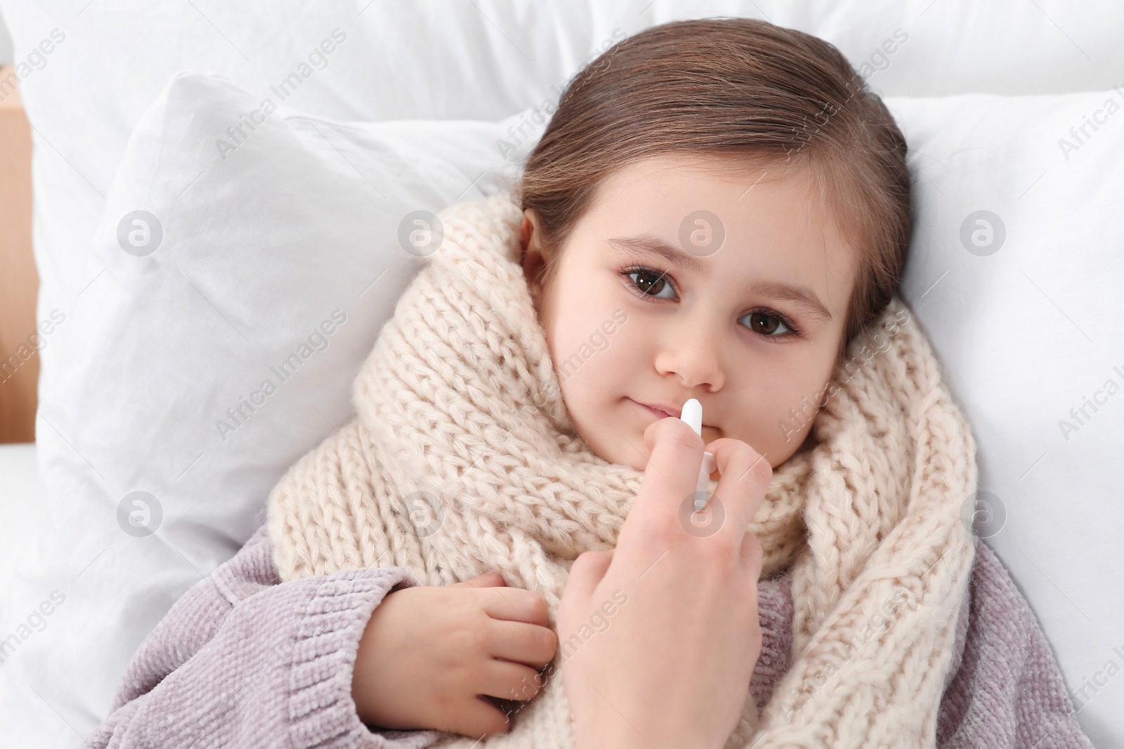 Photo of Mother using nasal spray to treat her little daughter on bed, above view