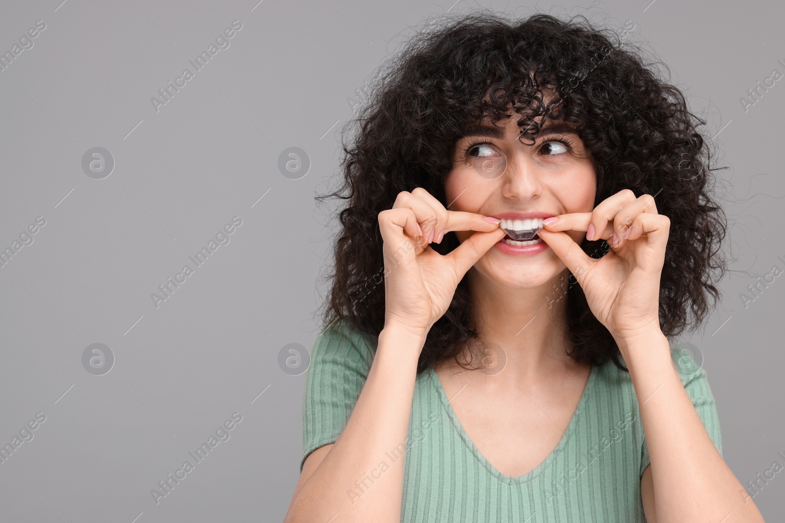 Photo of Young woman applying whitening strip on her teeth against grey background, space for text