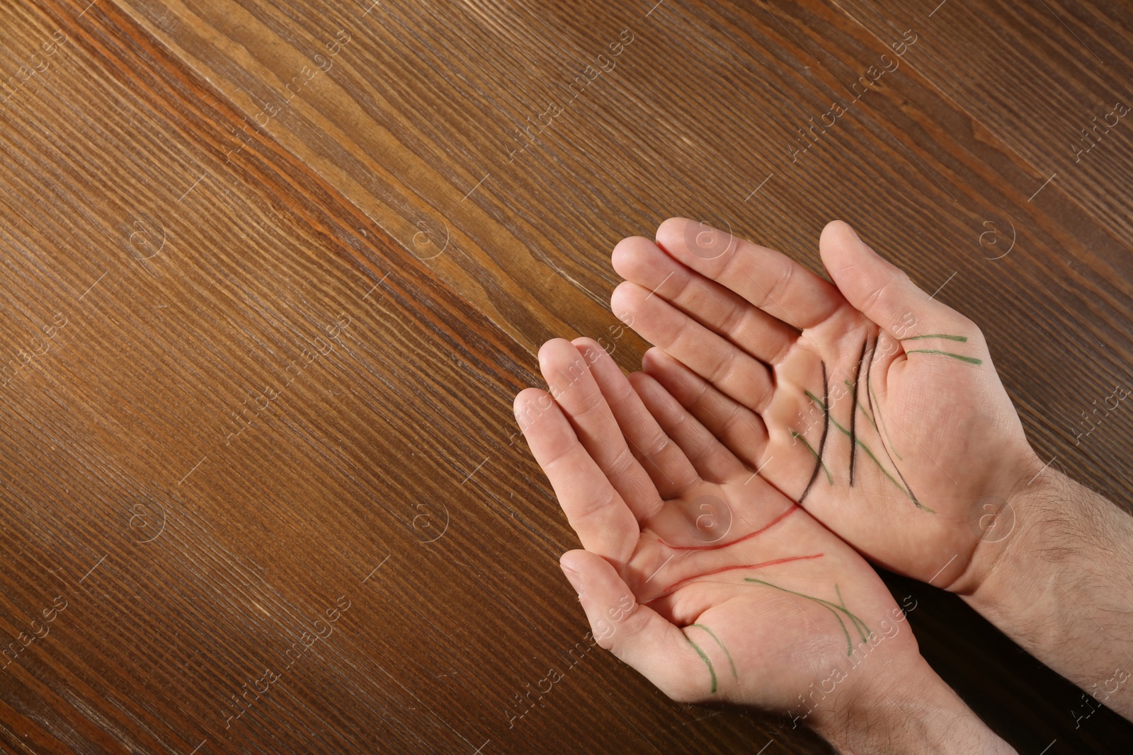 Photo of Top view of man showing palms with drawn lines on wooden background, space for text. Chiromancy and foretelling