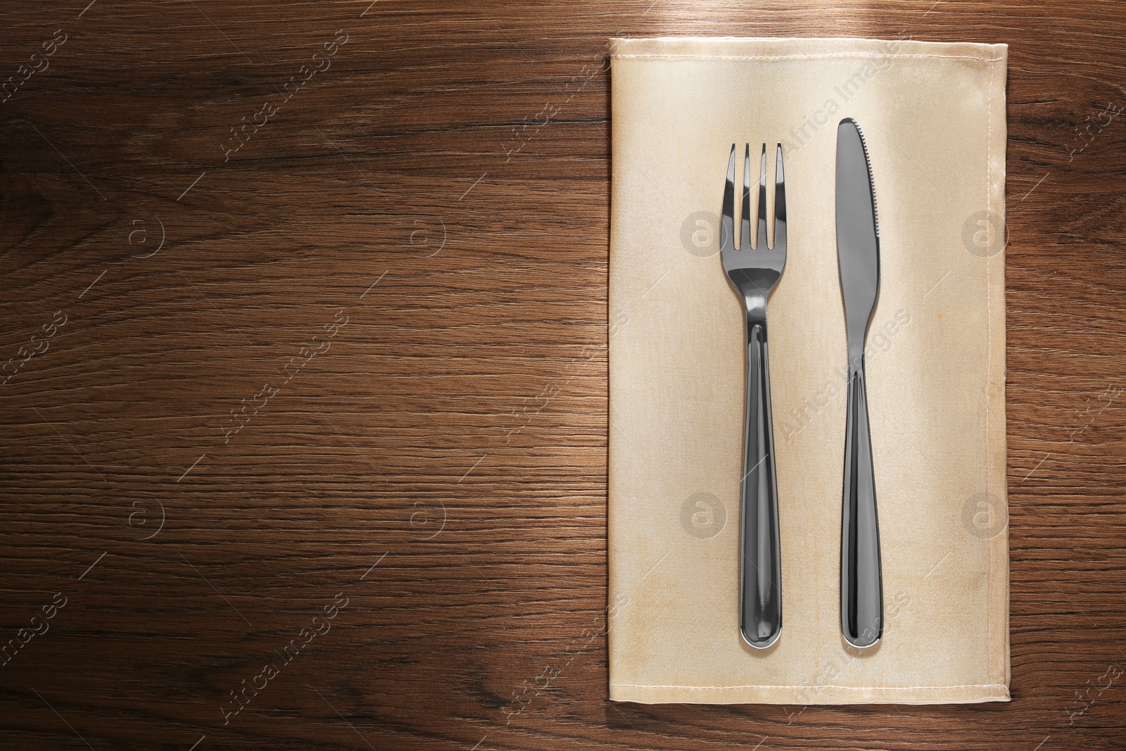Photo of Shiny fork, knife and napkin on wooden table, top view. Space for text