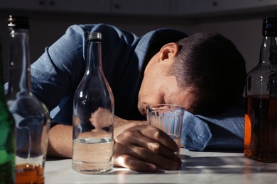 Addicted man with alcoholic drink sleeping at table in kitchen, closeup