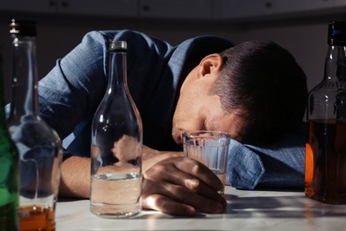 Photo of Addicted man with alcoholic drink sleeping at table in kitchen, closeup