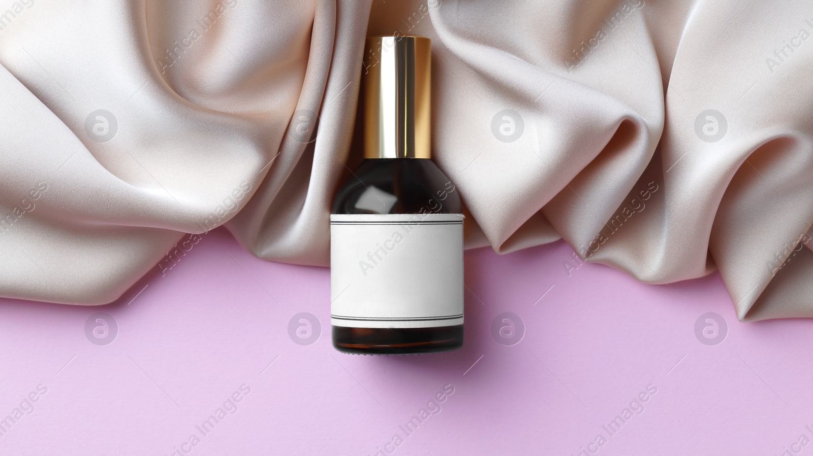 Photo of Luxurious bottle of perfume and beige silk on pink background, top view