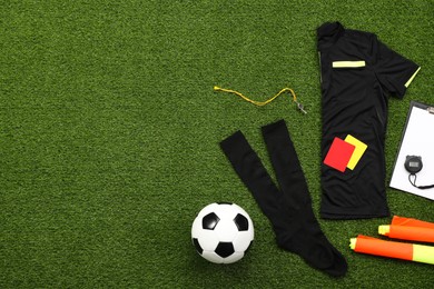 Uniform, soccer ball and other referee equipment on green grass, flat lay. Space for text