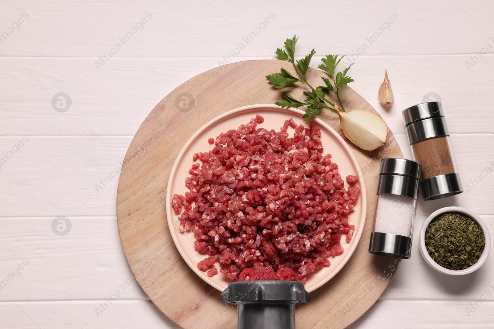 Photo of Manual meat grinder with beef mince, onion and spices on white wooden table, flat lay