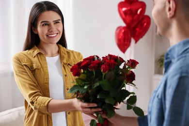 Photo of Young woman receiving beautiful bouquet of roses from her boyfriend indoors. Valentine's day celebration
