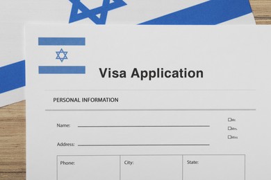 Photo of Immigration to Israel. Visa application form and flag on wooden table, top view