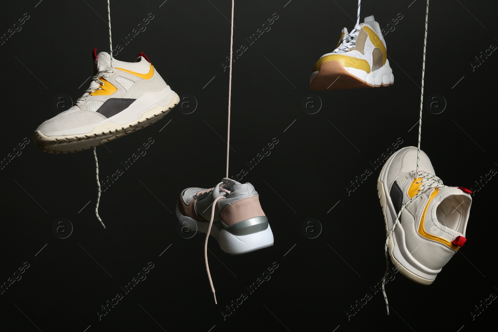 Photo of Different sneakers hanging on black background. Stylish shoes