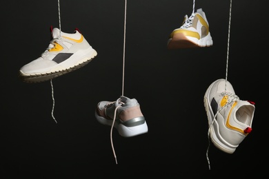 Photo of Different sneakers hanging on black background. Stylish shoes