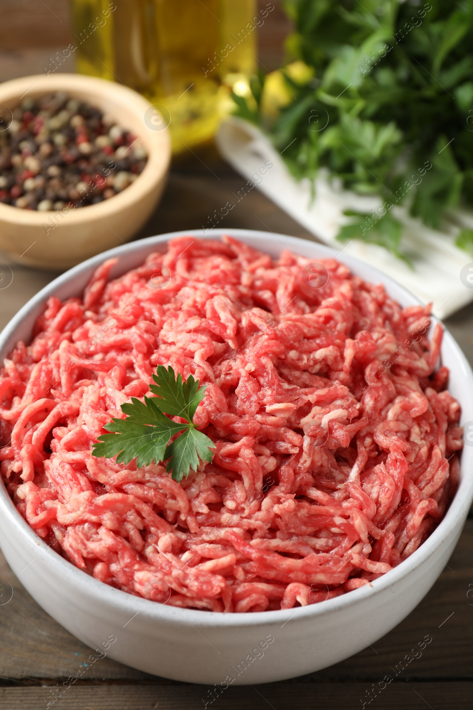 Photo of Raw ground meat in bowl, parsley, spices and oil on wooden table, closeup