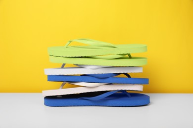 Photo of Stack of different flip flops on white table against yellow background
