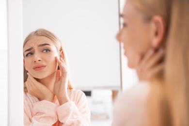 Young woman with eyelash loss problem looking in mirror indoors