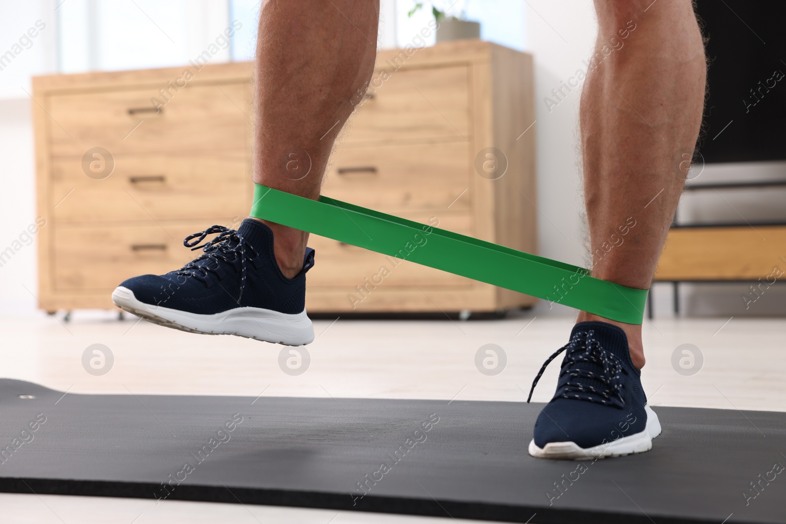 Photo of Athletic man doing exercise with elastic resistance band on mat at home, closeup