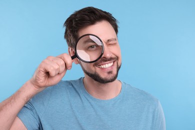 Photo of Happy man looking through magnifier glass on light blue background