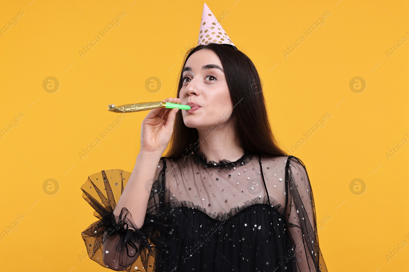 Photo of Woman in party hat with blower on orange background