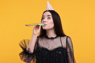 Woman in party hat with blower on orange background