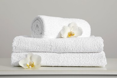 Photo of Clean soft white towels with flowers on table against light grey background