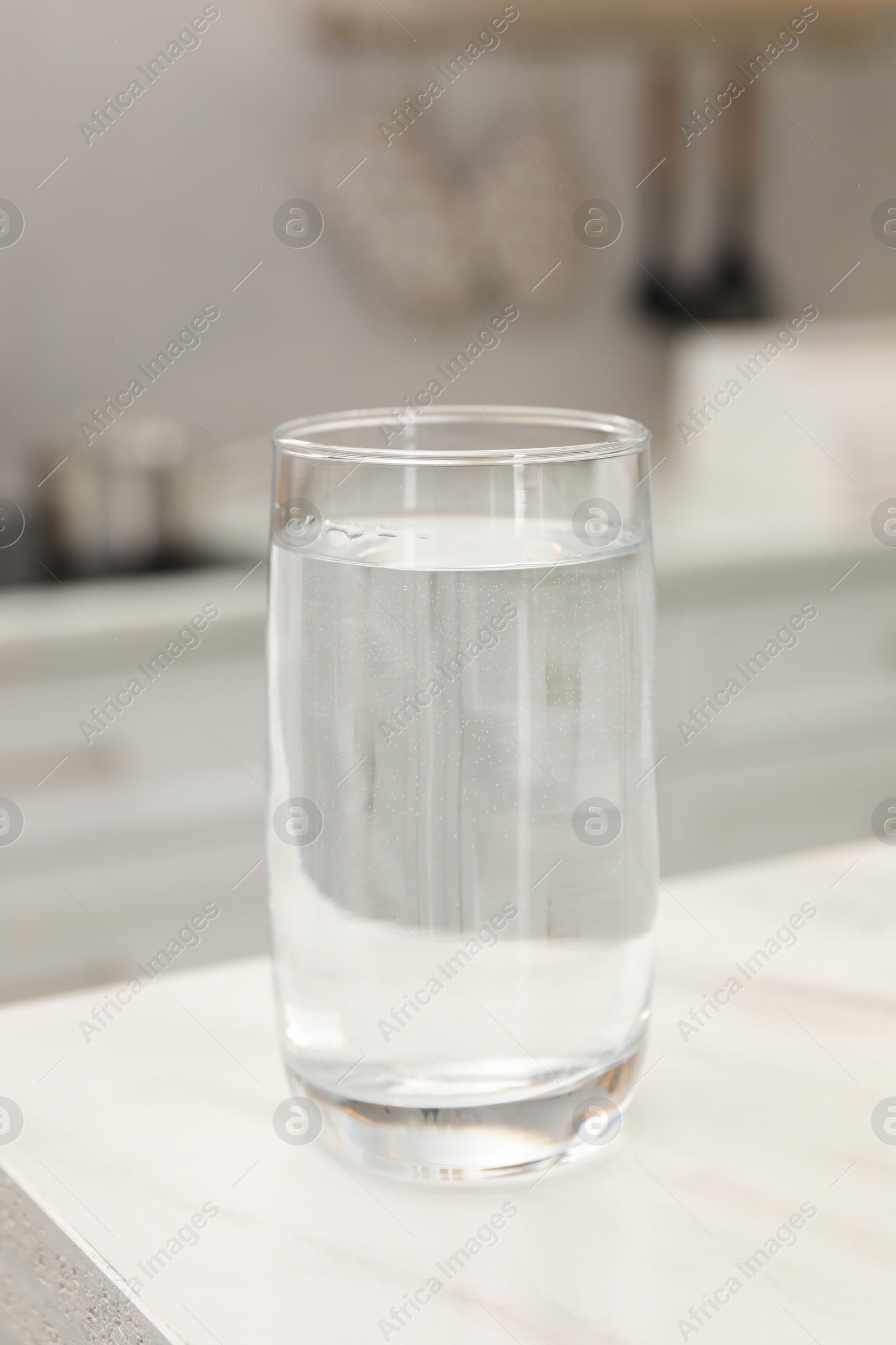 Photo of Glass with clear water on white marble table in kitchen