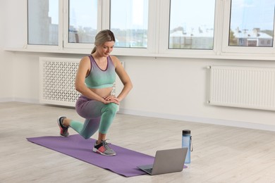 Photo of Online fitness trainer. Woman doing exercise near laptop at home