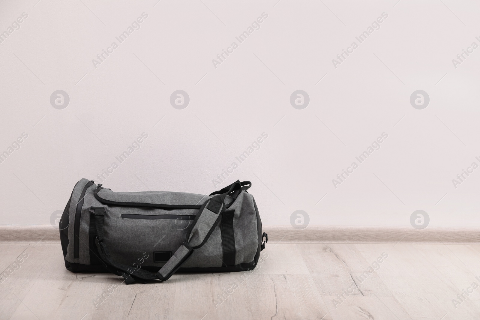 Photo of Grey sports bag on floor near white wall, space for text