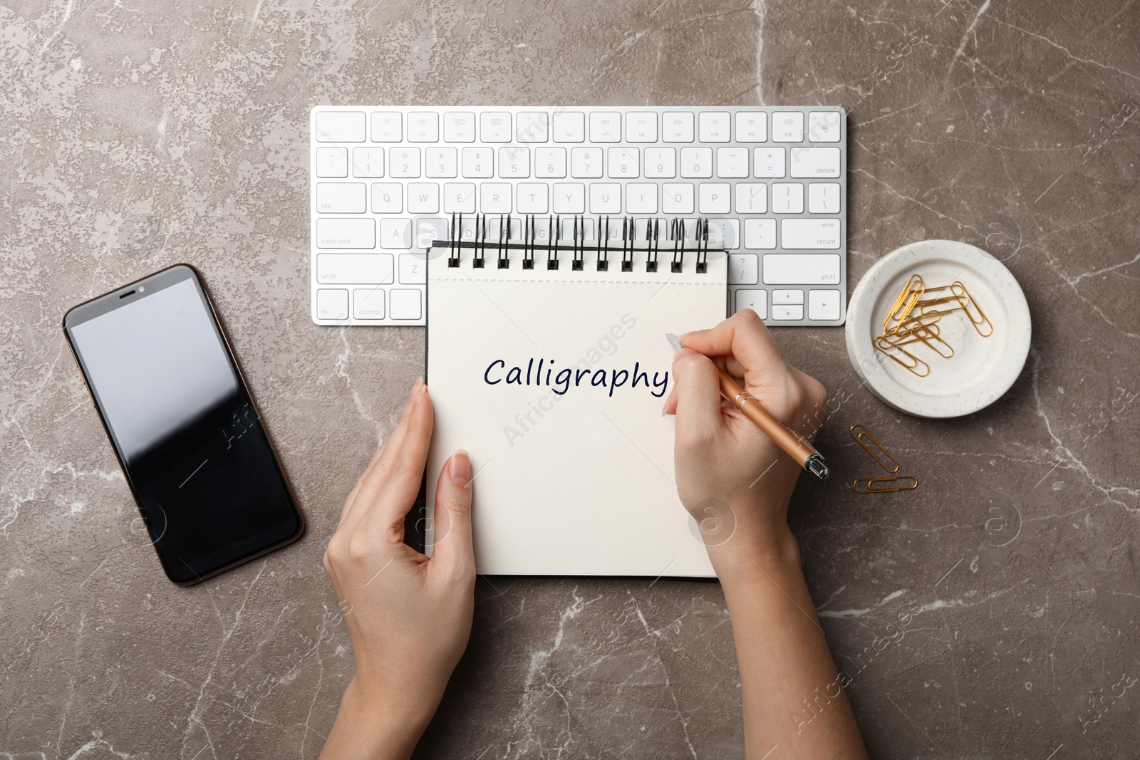 Image of Woman writing word Calligraphy in notebook at grey marble table, top view