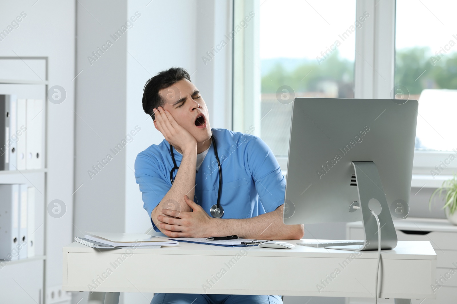 Photo of Exhausted doctor yawning at workplace in hospital