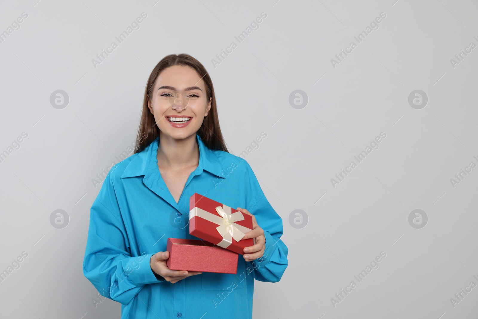 Photo of Portrait of emotional young woman opening gift box on grey background. Space for text