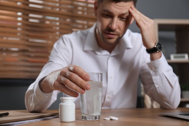 Photo of Man taking medicine for hangover at desk in office, focus on hand with glass