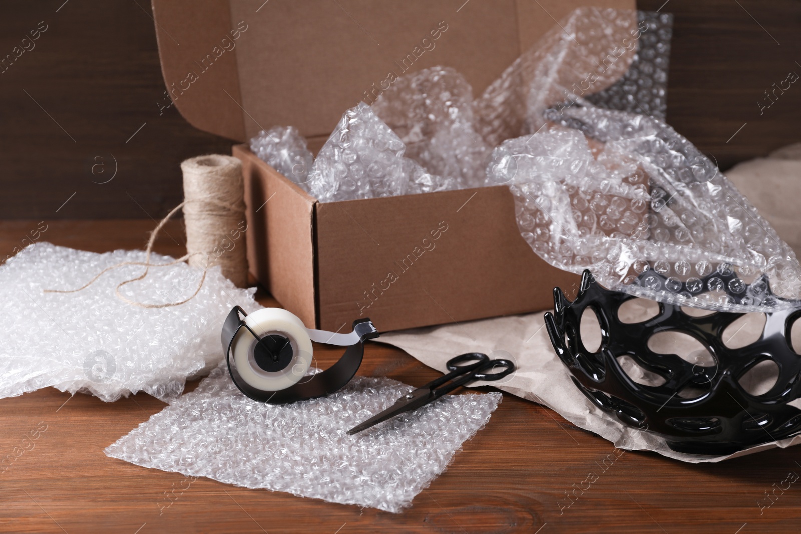 Photo of Beautiful ceramic bowl with bubble wrap near cardboard box and packaging materials on wooden table