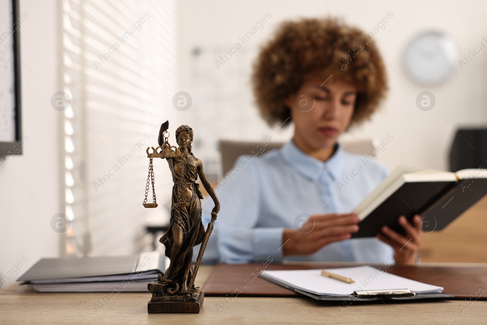 Photo of Notary with notebook at workplace in office, focus on statue of Lady Justice