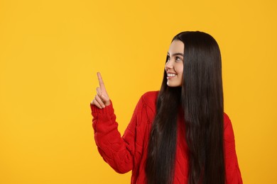 Photo of Teenage girl pointing at something on yellow background. Space for text