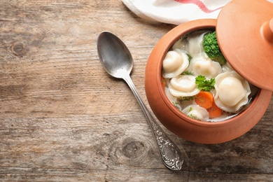 Photo of Pot of tasty dumplings with broth and vegetables served on wooden table, top view. Space for text