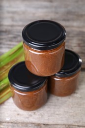 Photo of Jars of tasty rhubarb jam and stalks on wooden table, closeup