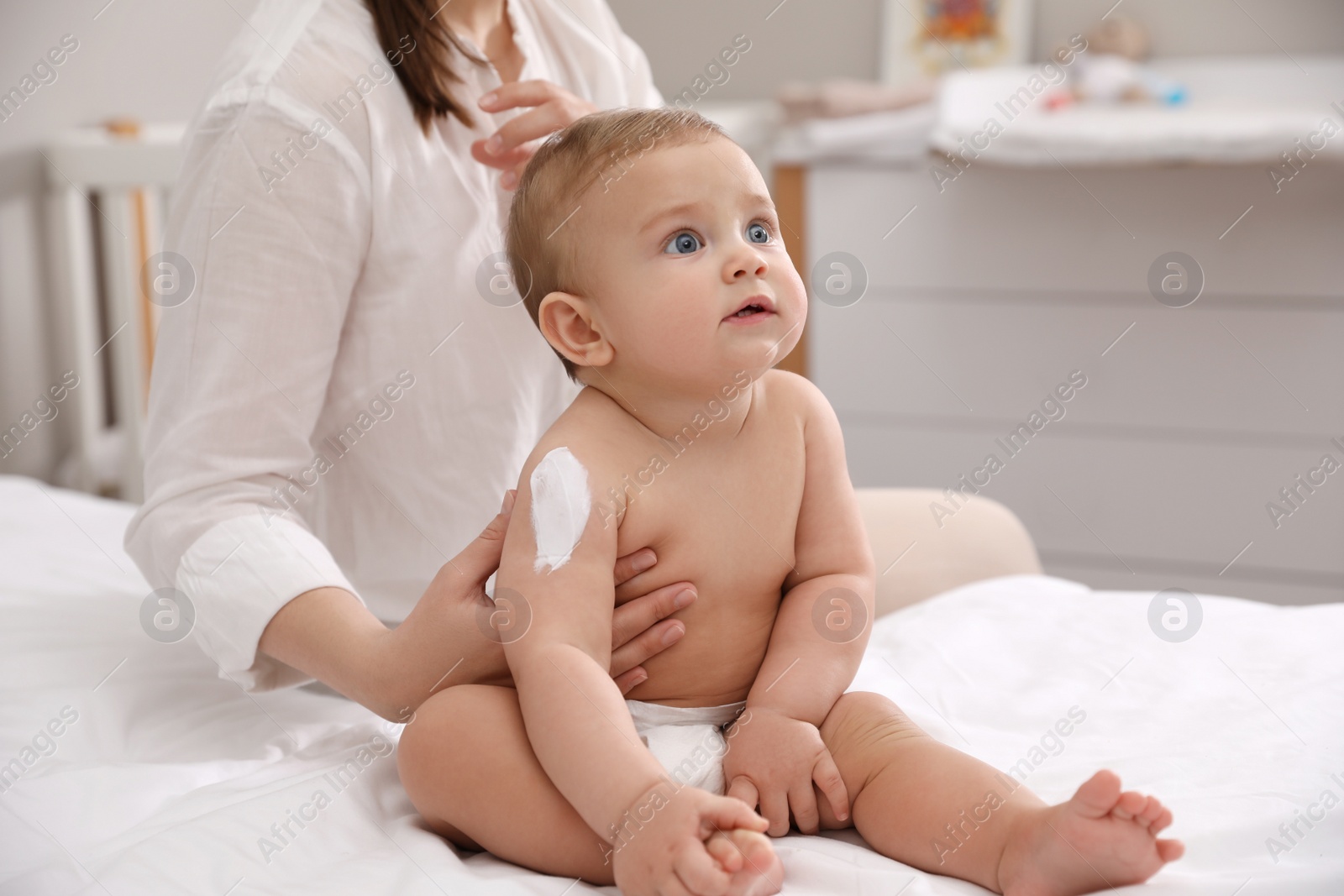 Photo of Mother applying moisturizing cream on her little baby at home, closeup