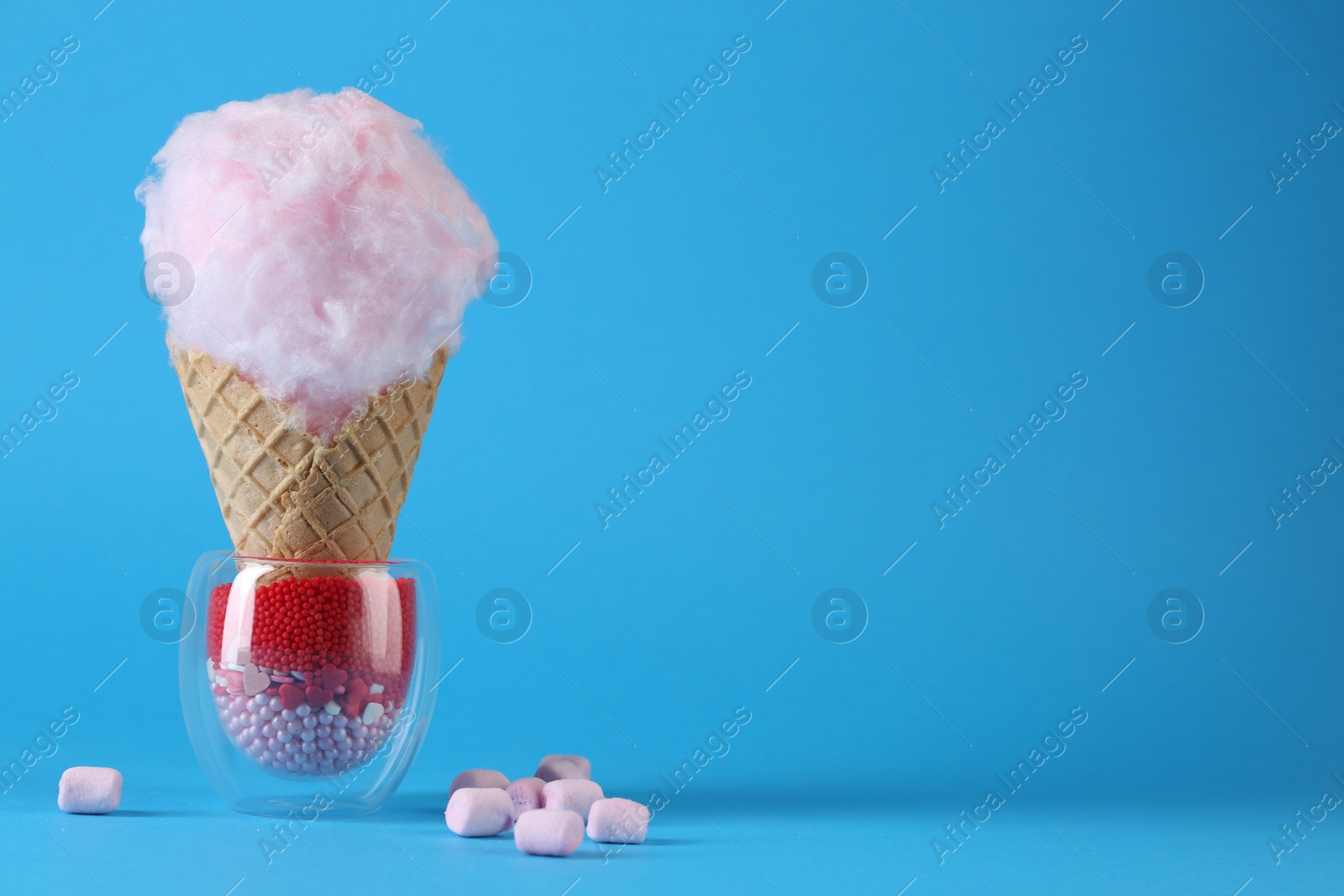 Photo of Sweet cotton candy in waffle cone and marshmallows on light blue background. Space for text