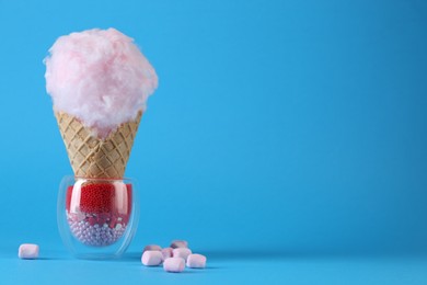 Photo of Sweet cotton candy in waffle cone and marshmallows on light blue background. Space for text