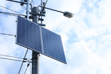 Solar panels on street light pole against cloudy sky, low angle view. Space for text