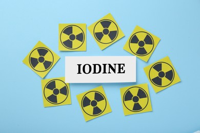 Paper note with word Iodine and radiation signs on light blue background, flat lay