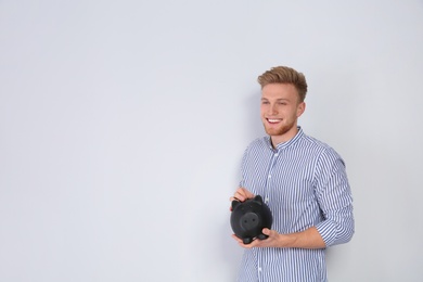 Young man putting coin into piggy bank on light background. Space for text