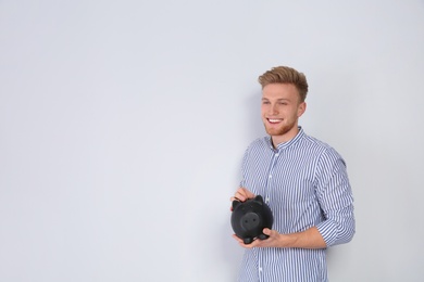 Photo of Young man putting coin into piggy bank on light background. Space for text