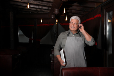 Photo of Senior business owner talking on phone in his restaurant
