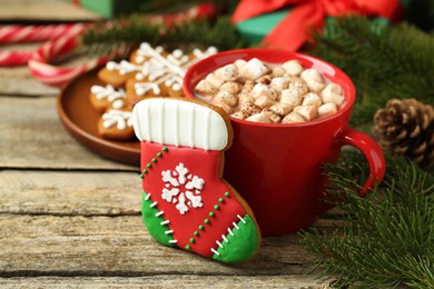 Tasty cookie in shape of Christmas stocking, cocoa with marshmallows and festive decor on wooden table, closeup. Space for text