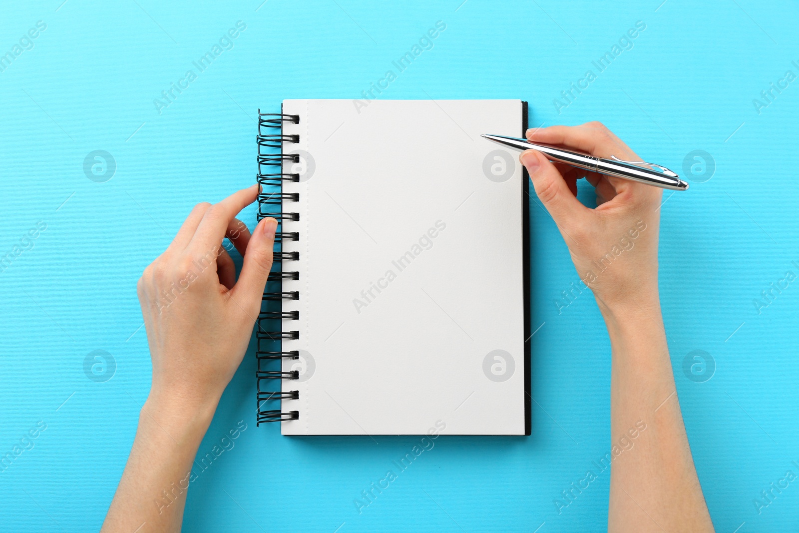 Photo of Woman writing in notebook on light blue background, top view