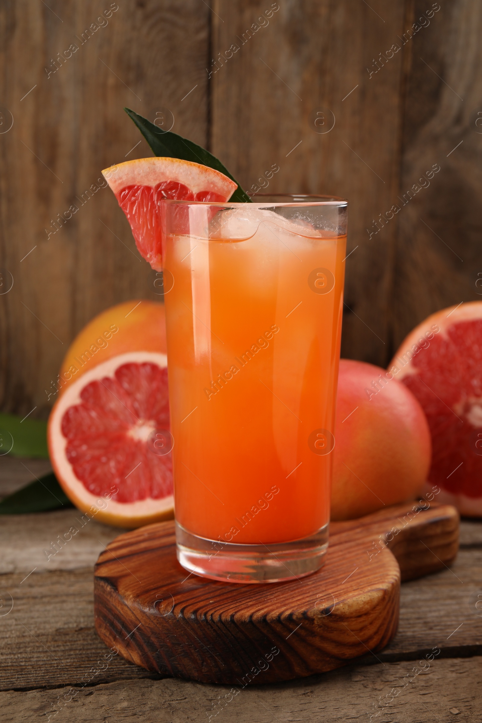 Photo of Tasty grapefruit drink with ice in glass and fresh fruits on wooden table