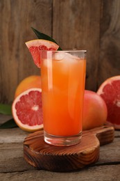 Photo of Tasty grapefruit drink with ice in glass and fresh fruits on wooden table