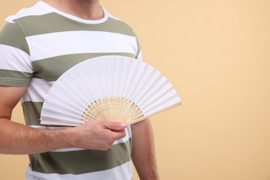 Photo of Man holding hand fan on beige background, closeup. Space for text
