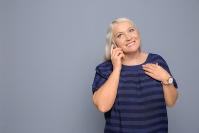 Photo of Mature woman talking on mobile phone against grey background